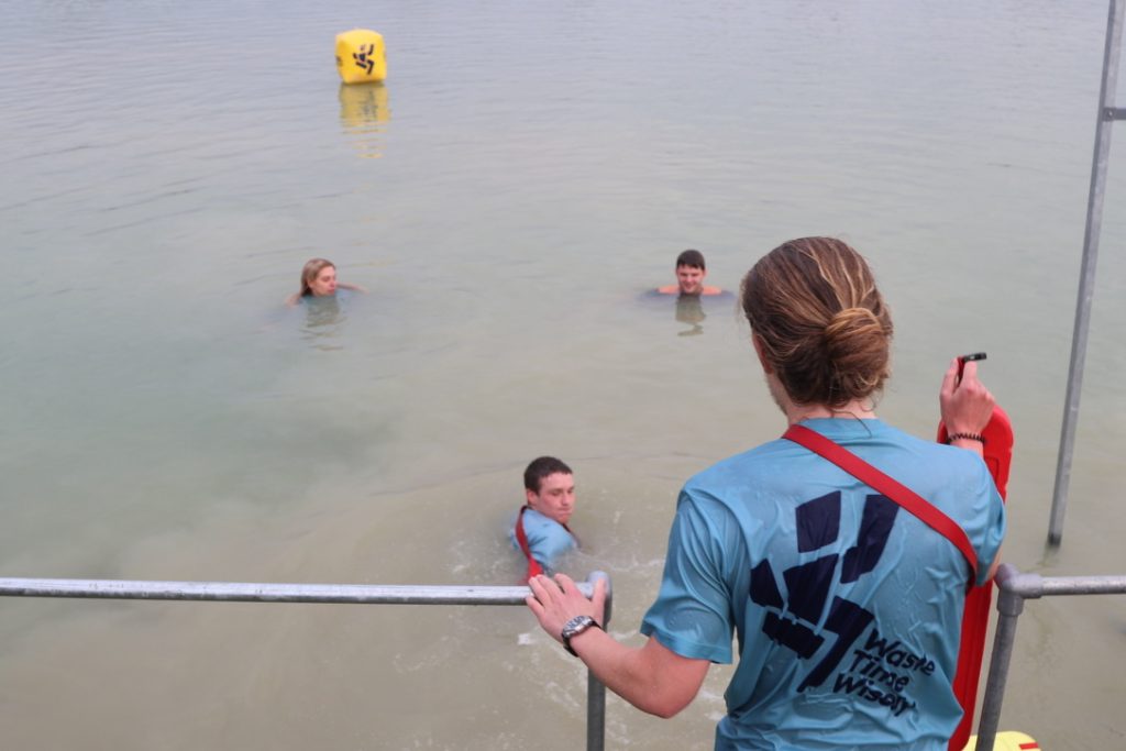 a lifeguard on the waters edge instructs other lifeguards that are in the water