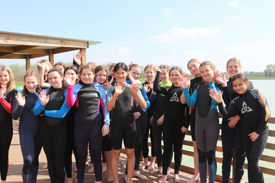 School group posing together in wetsuits by the lake.